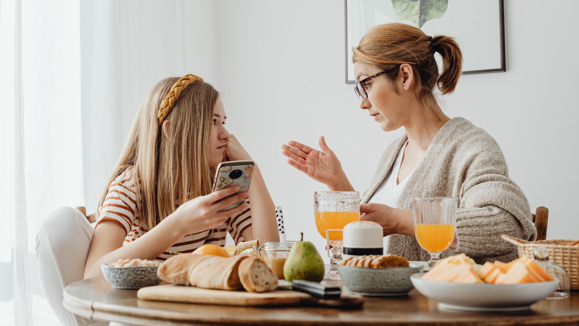 A mother talks with her teenage daughter while her daughter holds a smartphone.