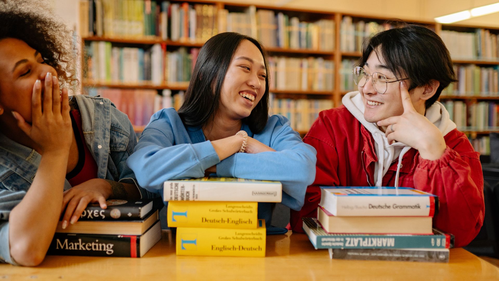 A group of teenage students talks and laughs while sitting in a library.