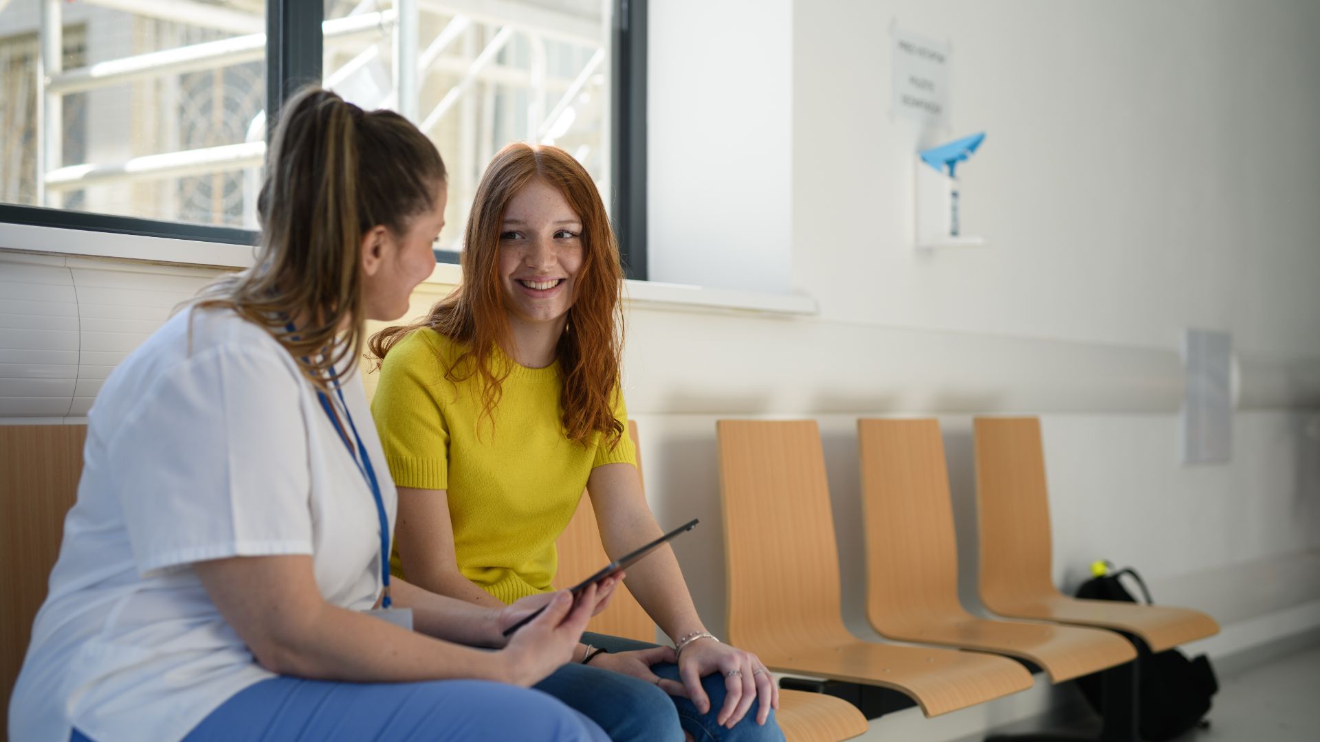 A teenage daughter smiles at her mother while her mother holds a tablet.