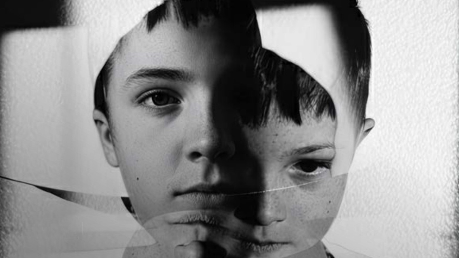 A black and white image showing the faces of two young boys looking pensive.