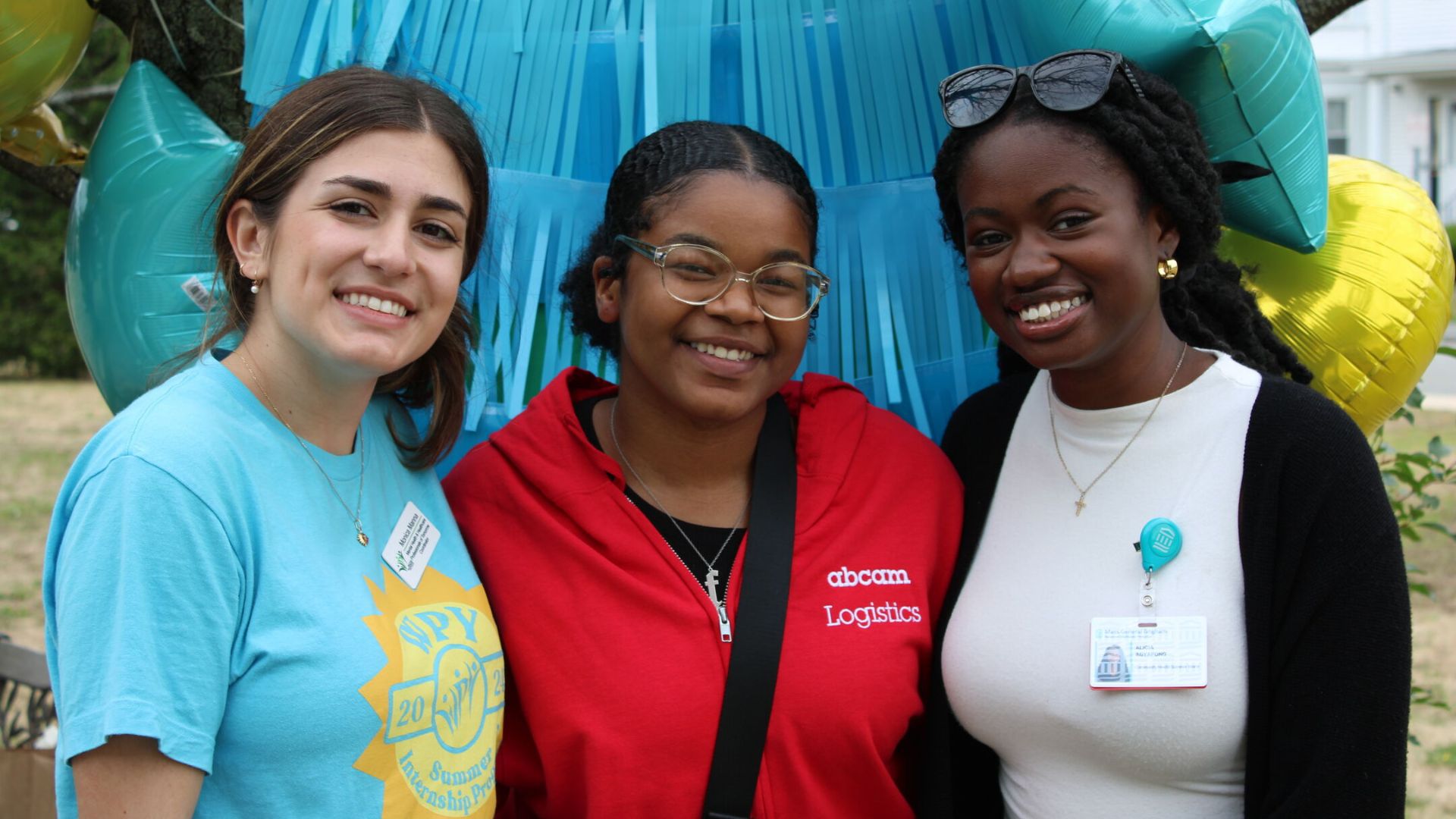 Three young women smiling while standing in front of festive decorations.