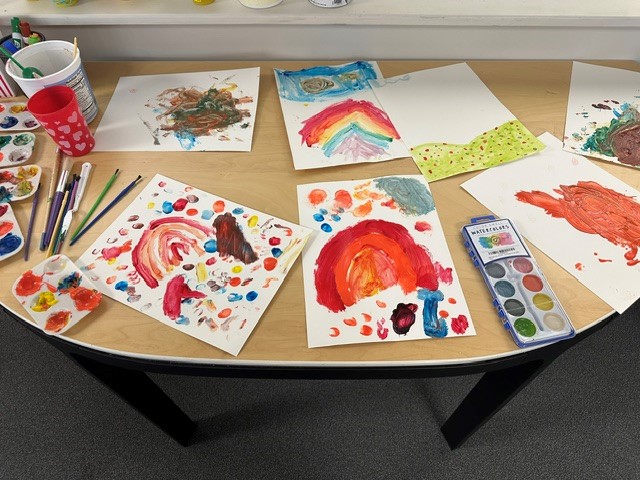 Paintings, drawings, and art supplies spread out on a table.