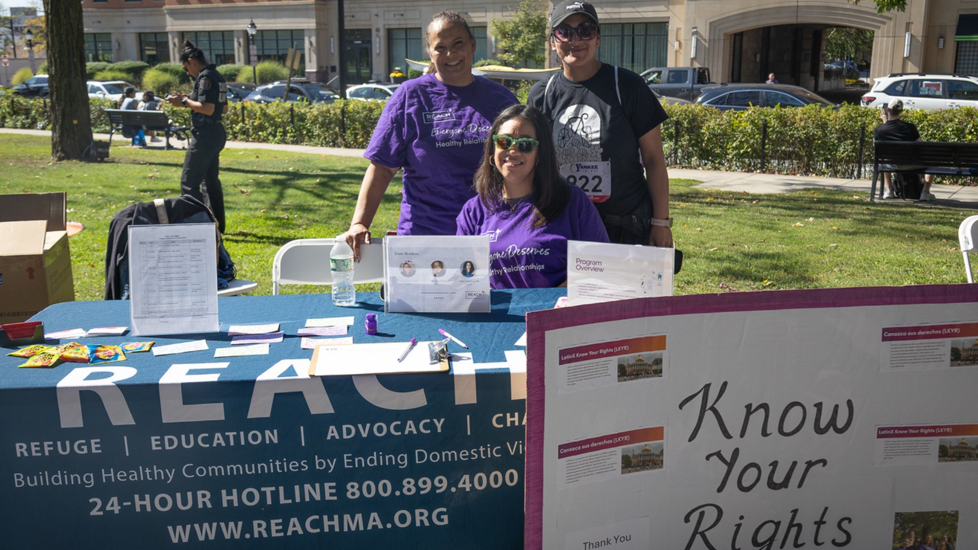 Three women smiling while sitting at a table with REACH language and a 'Know Your Rights' sign.